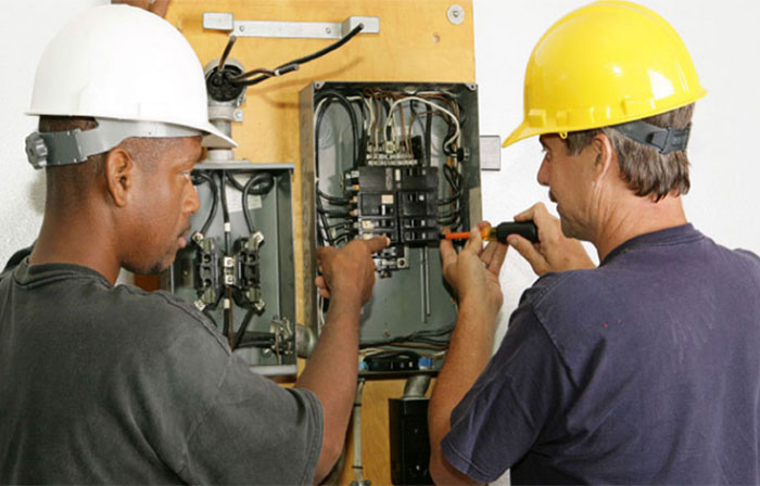 Two men with hard hats looking at panel