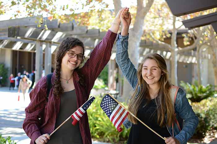 Two female students holding flags and hands up in the air