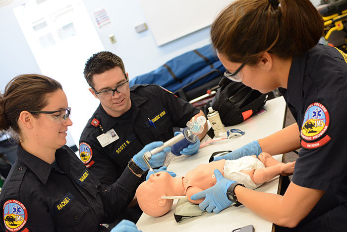 two females and one male student practicing cpr on a baby doll