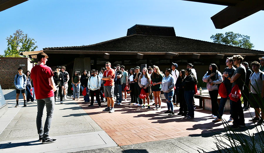 student tour guide with about 40 people in front of a hut shaped building